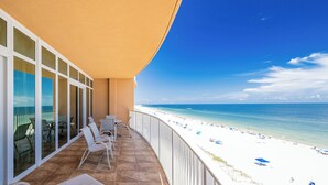 Un balcón con vista a una playa, sillas blancas y una mesa.