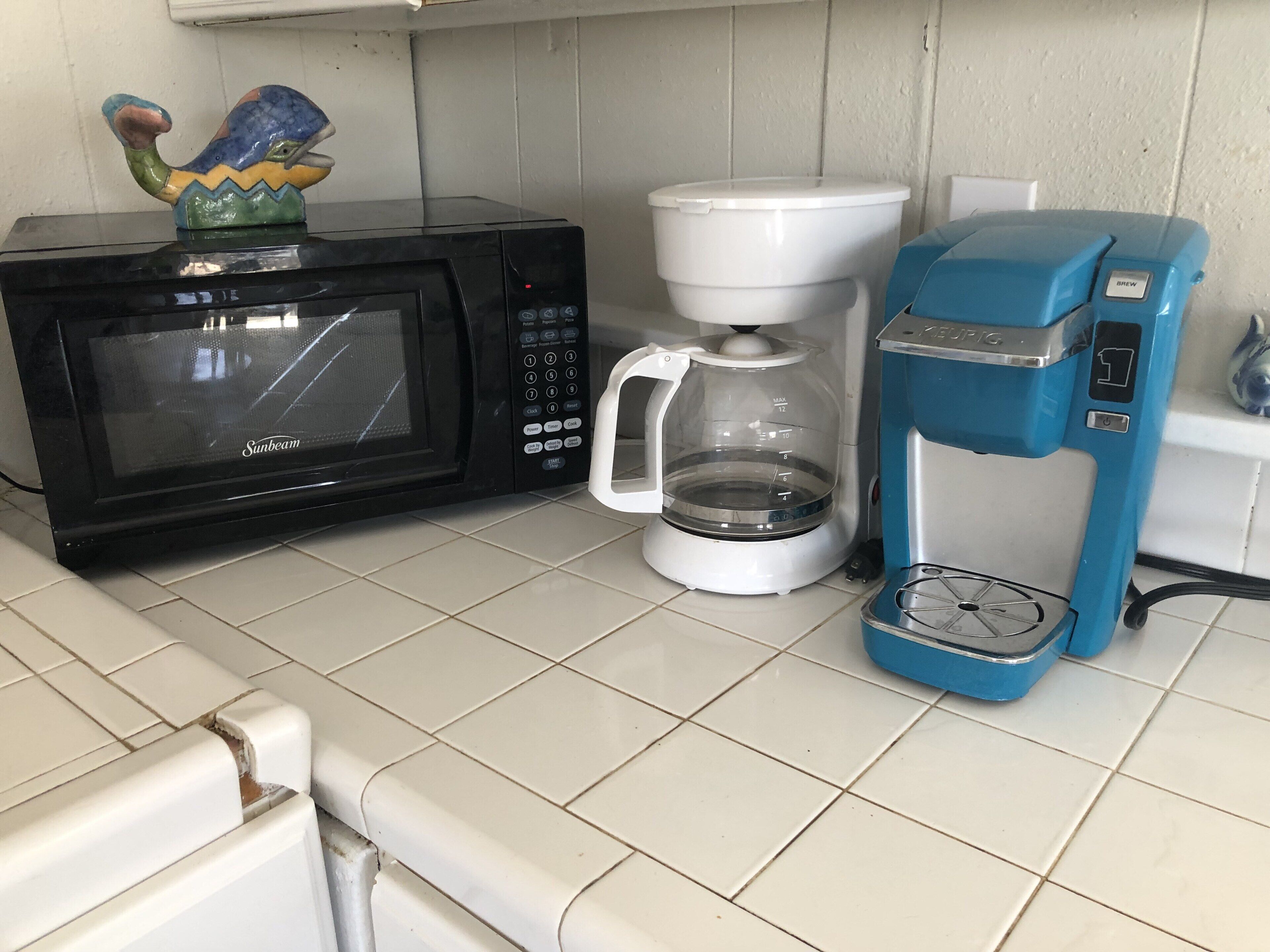 Eine Küche mit einer schwarzen Mikrowelle, einer weißen Kaffeemaschine und einer blauen Kaffeemaschine.