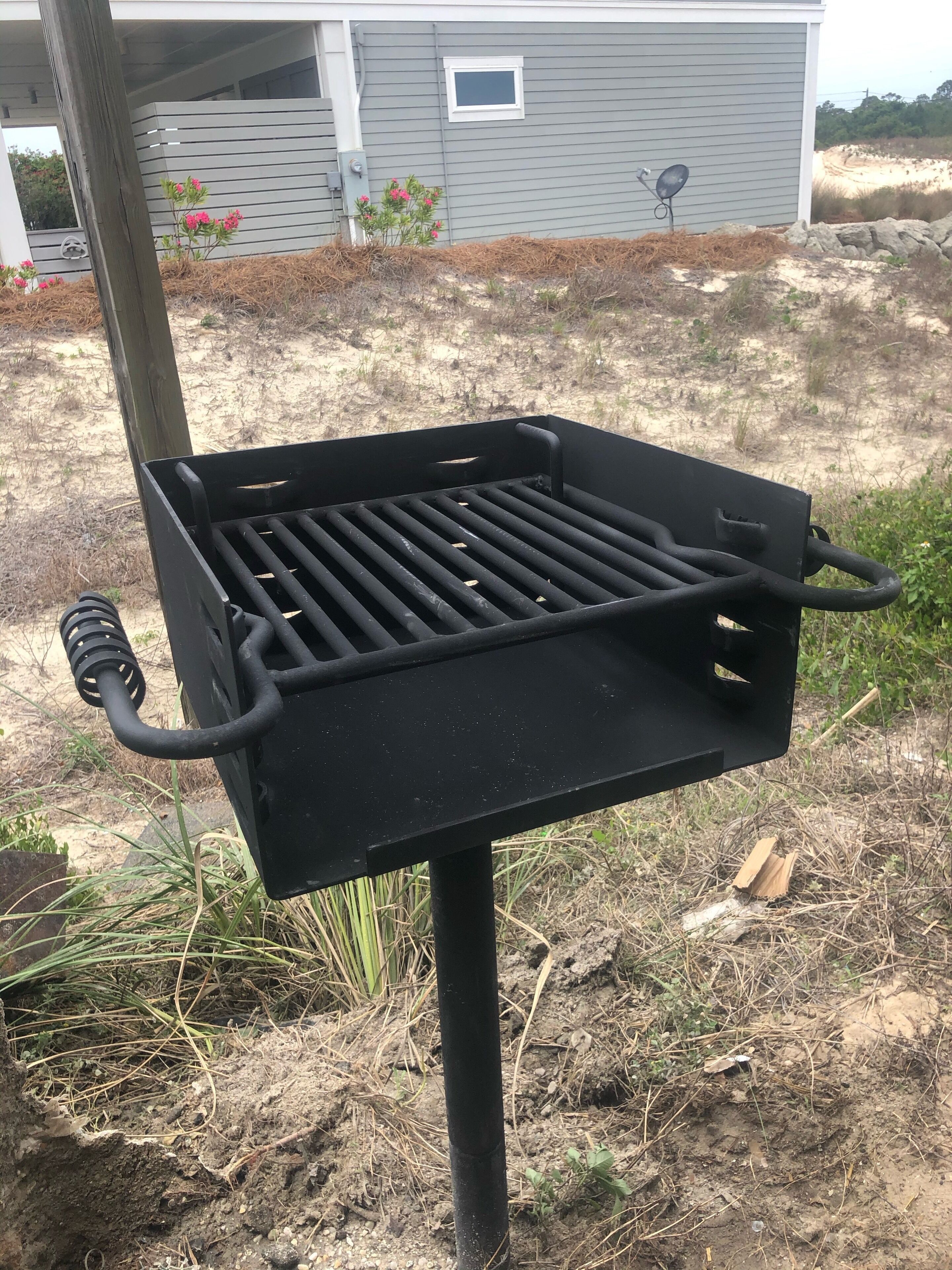 A black barbecue grill with a metal grate, a handle, and a hose, set outdoors with a house in the background.