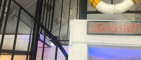 A lifebuoy hanging from a railing, a sign reading "Captain's Loft", and a staircase with black railings.