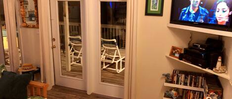 A living room with a television, a bookshelf, a rocking chair, and a sliding glass door leading to a balcony.