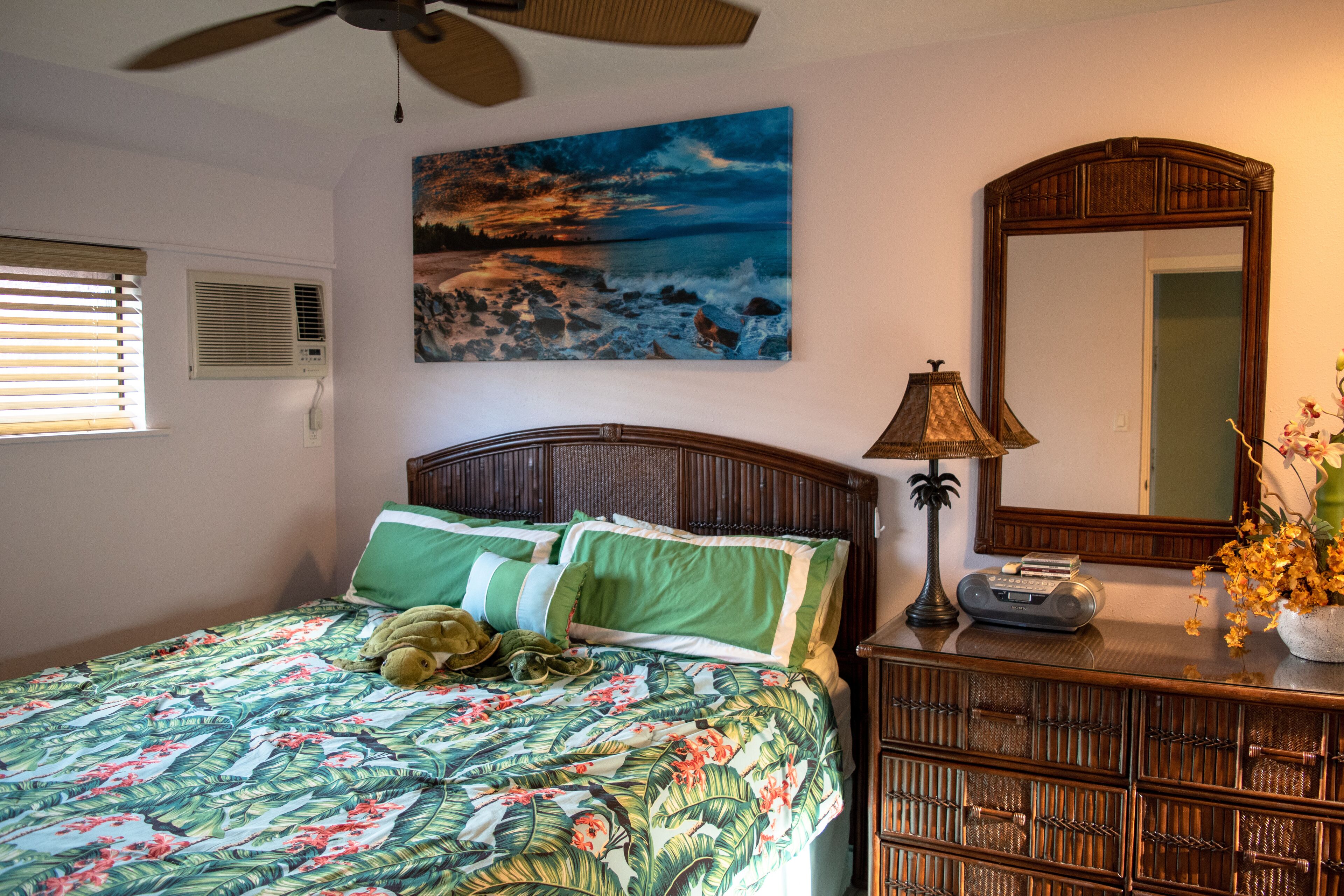 Une chambre à coucher comprenant un lit, une table de chevet, une lampe, un miroir, un tableau et une fenêtre avec des stores.