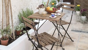An outdoor patio with a wooden table and chairs, surrounded by potted plants and a white wall. - Athenian House in Plaka (Athens)