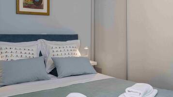 A neatly made bed with white linens and pillows, a framed artwork on the wall, and a hanging light fixture.
