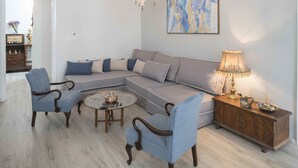 A living room with a sectional sofa, two armchairs, a coffee table, a side table with a lamp, and a decorative piece on the wall. - Athenian House in Plaka (Athens)