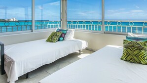 A room with two beds, each with a white bedspread and colorful pillows, large windows with a view of the ocean and a distant cityscape. - A View to Die for! 3 bedroom 3 bath on the sand at Waikiki Beach (Honolulu)