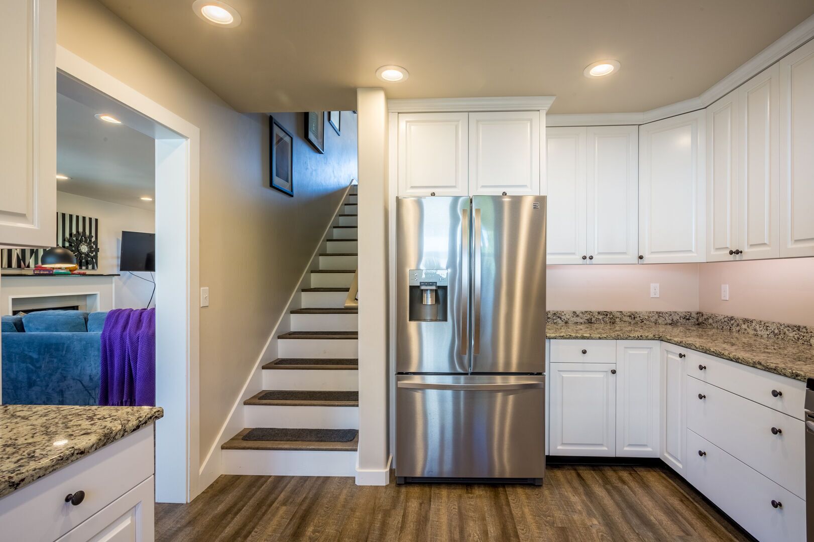 Cocina moderna con armarios blancos, refrigerador de acero inoxidable, encimeras de granito y una escalera de madera.