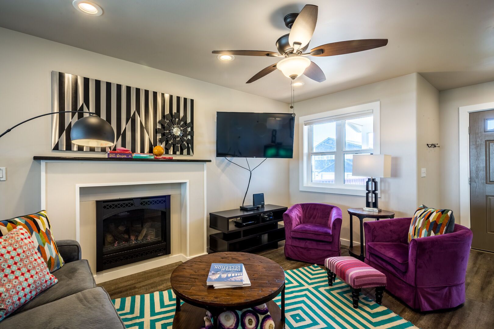 A modern living room with a fireplace, a ceiling fan, a TV, and purple furniture.