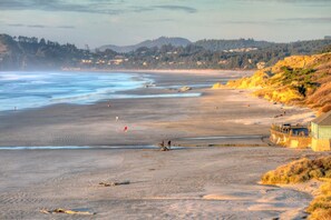 A wide beach with a wooden pier extending into the water, surrounded by hills and sparse vegetation. - Nye Beach, Hot tub, Dog friendly, Hip Decor, Walk to Beach! (Newport)