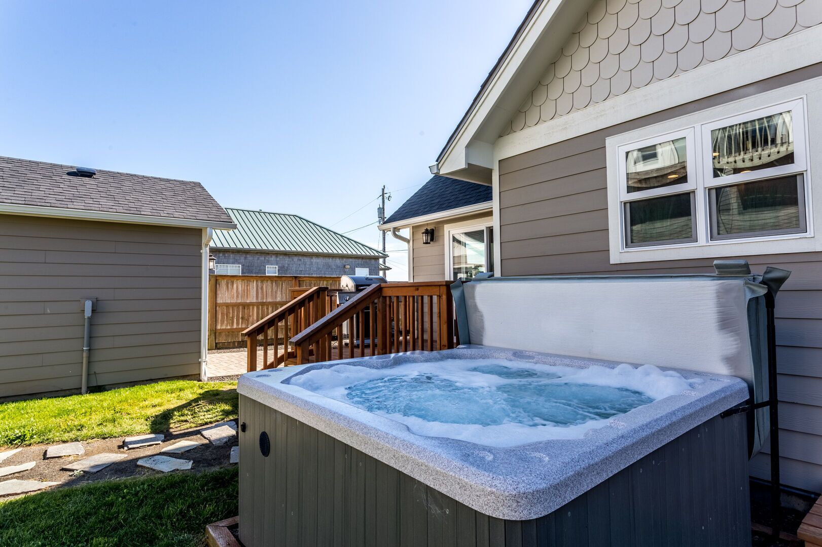 Un jacuzzi dans un jardin, avec une terrasse en bois et une maison en arrière-plan.