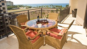 A balcony with wicker furniture, a glass table, and a view of the ocean.