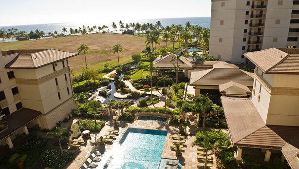 A resort with a central pool, palm trees, and a view of the ocean.