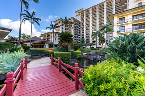 A red bridge leading to a modern hotel with multiple balconies and a landscaped garden. - Luxury Ko Olina Beach Villas: Panoramic Ocean View 3BR (Kapolei)