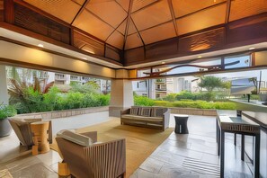 A modern interior with a high ceiling, a seating area with a sofa and chairs, and a view of greenery outside.