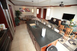 A modern kitchen with a central island, a dining area with chairs, a sofa, and a television.