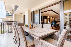 Un espace repas moderne avec une longue table et des chaises en osier, un balcon doté d’une balustrade et une vue sur l’intérieur du bâtiment.