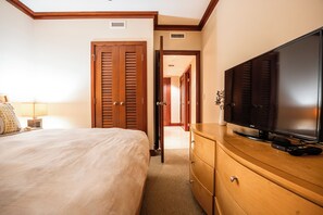 A hotel room with a bed, a television on a wooden dresser, and a door leading to another room.