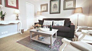 A living room with a sofa, coffee table, and two lamps. There are framed pictures on the wall and a potted plant on the side table. - Eiffel-Invalides, New & Elegant  (Paris)