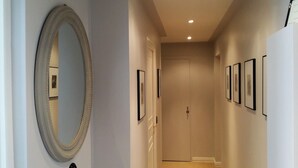 A hallway with a large mirror, framed pictures, and a closed door at the end. - Eiffel-Invalides, New & Elegant  (Paris)