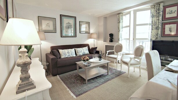 A living room with a sofa, coffee table, and chairs. There are framed pictures on the wall and a fireplace. - Eiffel-Invalides, New & Elegant  (Paris)