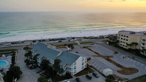 A coastal hotel with a parking lot, a pool, and a view of the beach and ocean.