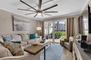 A spacious living room with a ceiling fan, a sofa set, a coffee table, and a television.