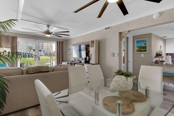 Ein modernes Wohnzimmer mit einem Glastisch, weißen Sofas und einem Deckenventilator.