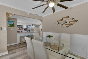 A dining area with a glass table, white chairs, and a ceiling fan.
