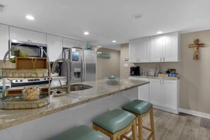 Een moderne keuken met witte kasten, roestvrijstalen apparatuur en een marmeren eiland met krukken.