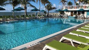 A pool area with lounge chairs and umbrellas, palm trees, and a clear sky. - P63 - Beautiful, waterfront duplex, walking distance to The Cabana Club! (Key Colony Beach)