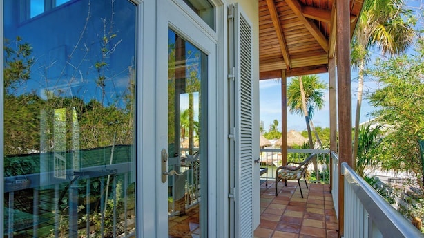 A balcony with a view of palm trees and a thatched-roof structure. - P63 - Beautiful, waterfront duplex, walking distance to The Cabana Club! (Key Colony Beach)