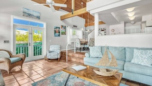 A spacious living area with a high ceiling, a dining area, and a balcony with a view of greenery. - P63 - Beautiful, waterfront duplex, walking distance to The Cabana Club! (Key Colony Beach)