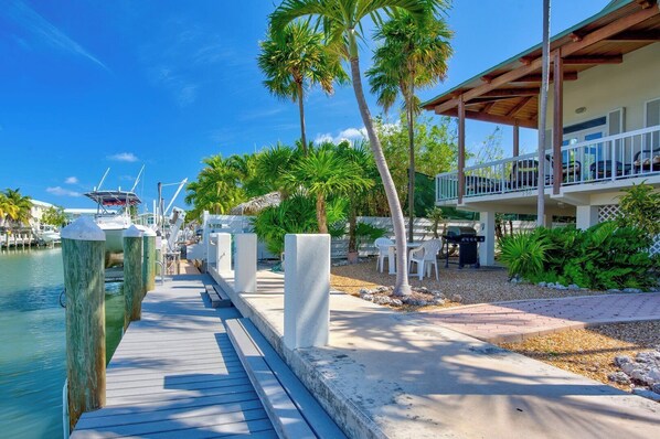 A waterfront property with a wooden dock, palm trees, and a covered outdoor seating area. - P63 - Beautiful, waterfront duplex, walking distance to The Cabana Club! (Key Colony Beach)