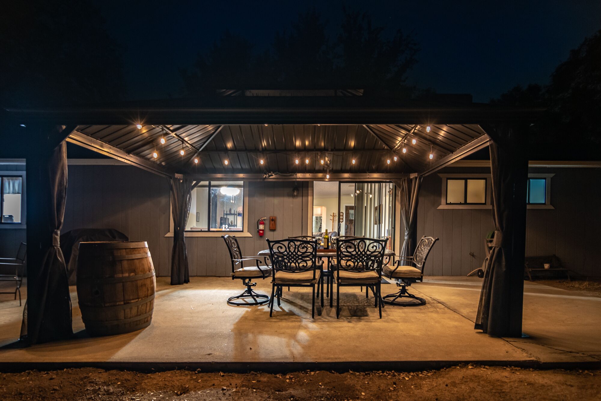 An outdoor covered patio with a table and chairs, a barrel, and a fire extinguisher.