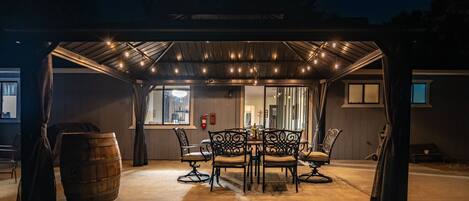 An outdoor covered patio with a table and chairs, a barrel, and a fire extinguisher.