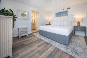 Un dormitorio con cama, mesitas de noche, lámpara de pared, un cuadro enmarcado y una planta.