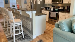 Eine moderne Küche mit weißen Schränken, einer Granit Arbeitsplatte, Edelstahlgeräten und einer Bar mit weißen Barhocker.