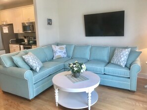 Una sala de estar con un sofá seccional azul claro, una mesa de centro redonda blanca y un televisor de pantalla plana montado en la pared.