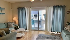 Ein Wohnzimmer mit einer Couch, einem Couchtisch und einem Teppich. Ein Balkon mit Geländer und Blick auf ein Gebäude ist vorhanden.