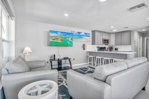 A modern living room with a sofa, a coffee table, and a TV. There is a kitchen area with a microwave and a sink. - M123 - Cabana Beach Duplex! Premier location across the street from Cabana Beach Club! (Key Colony Beach)