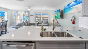 Une cuisine moderne dotée d’un grand îlot central, d’appareils électroménagers en acier inoxydable et offrant une vue sur la mer par les fenêtres.