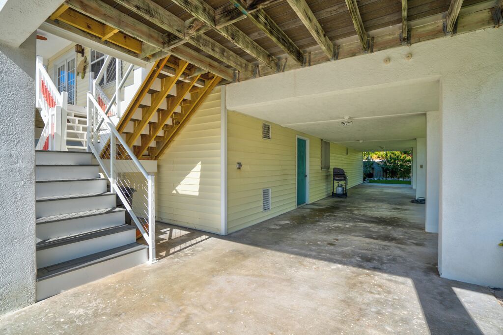A covered outdoor area with a concrete floor, a staircase with white railings, and a wooden ceiling structure.