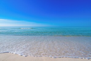 Une plage avec une eau d’un bleu limpide et un rivage sablonneux.
