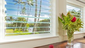 Une chambre avec vue sur les palmiers et un paysage tropical, visible à travers une fenêtre munie de stores.