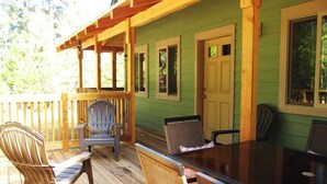 Une terrasse en bois avec une table à plateau de verre et des chaises en osier, un mur de serre végétalisé et une porte.