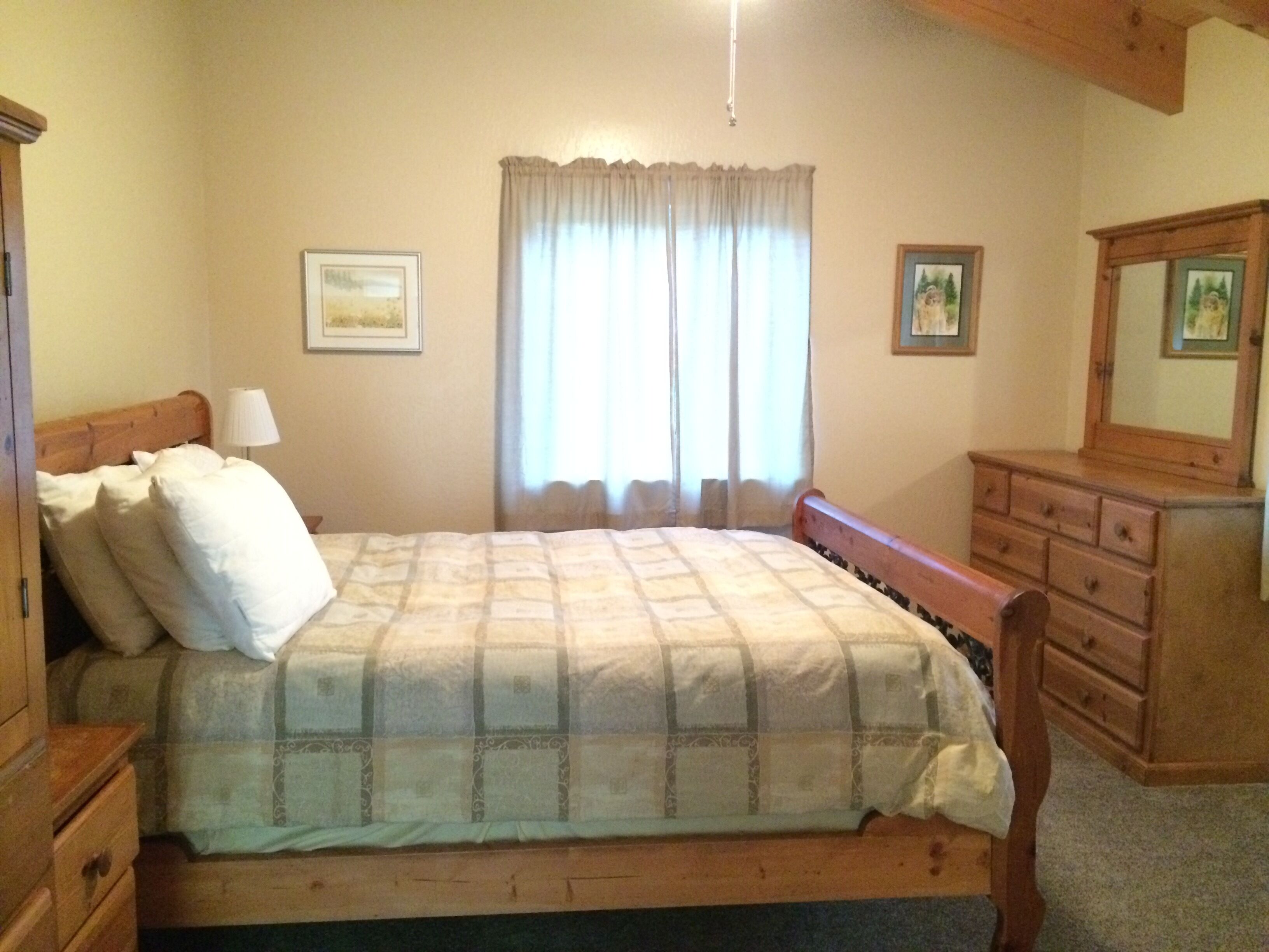 A bedroom with a bed, a dresser, a mirror, and two framed pictures on the wall.