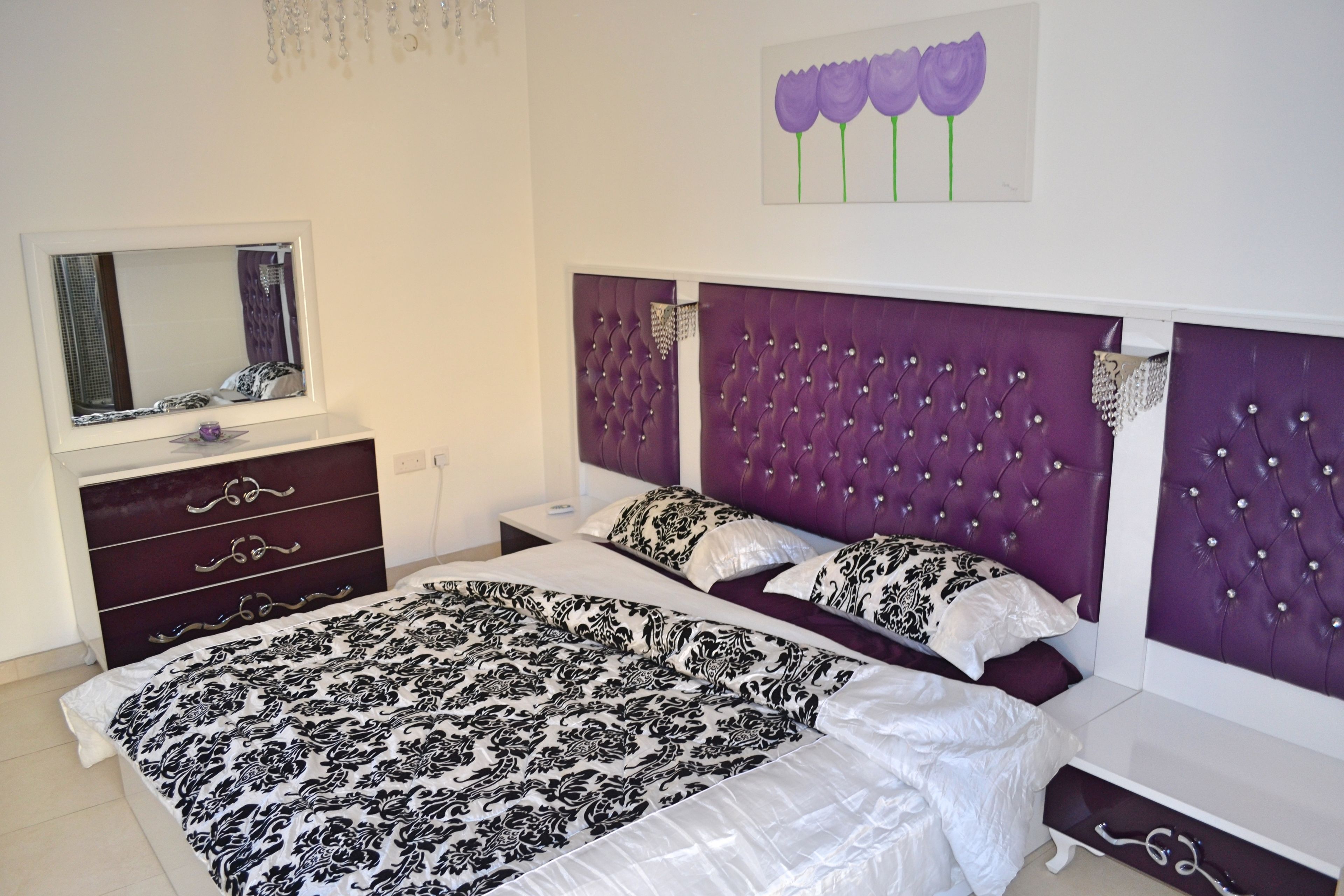 A bedroom with a large bed, a dresser, a mirror, and a purple headboard.