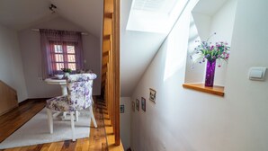 A staircase leading to a loft bedroom with a wooden floor, a white chair, a small table, and a purple vase with flowers on a shelf. - Studios Belvi (Kotor)
