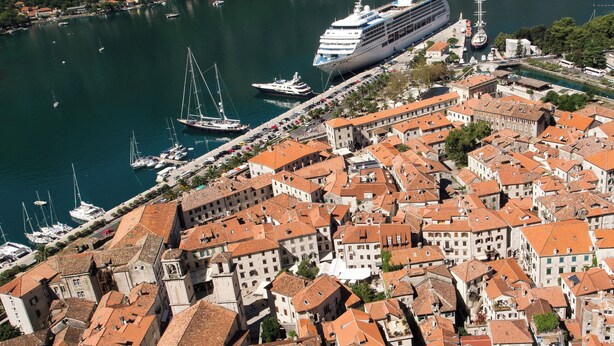 A cruise ship docked at a port with a historic town in the background. - Studios Belvi (Kotor)