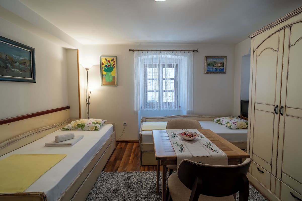 A small, well-lit room with two beds, a table with a bowl, and a wardrobe.